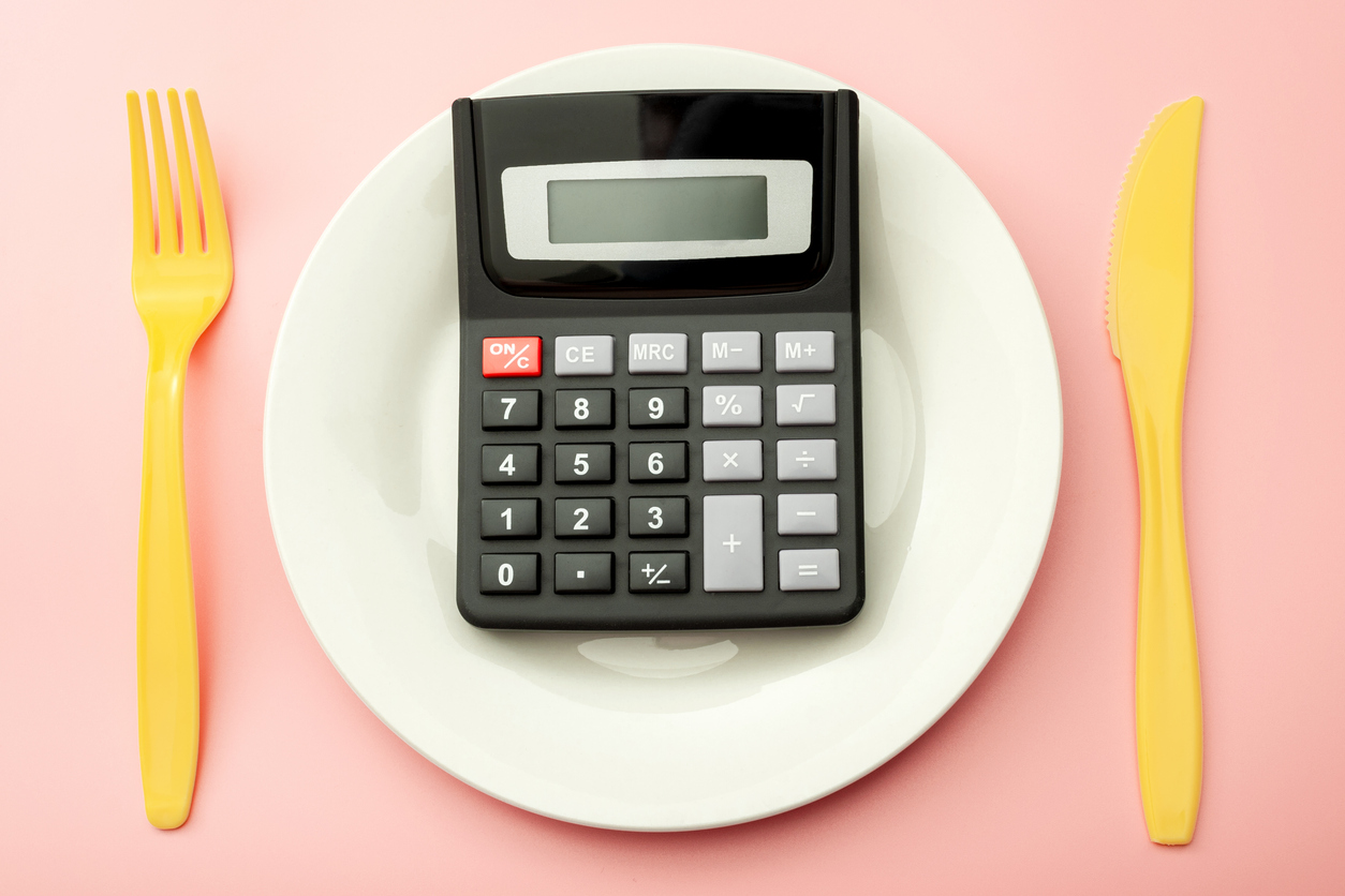 Calculate expensive food spending costs, counting calories and weight loss program concept with calculator on empty plate, yellow fork and knife isolated on pink background