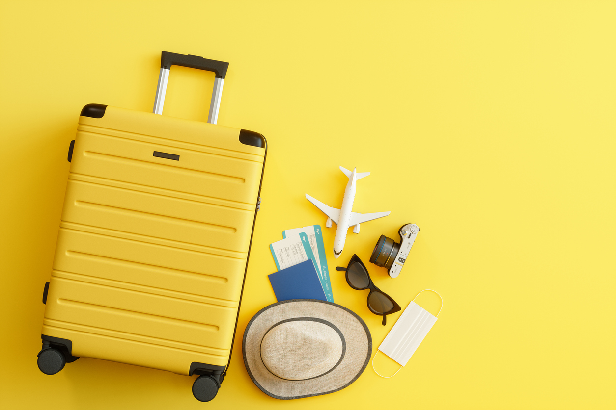 Medical Mask, Suitcase with Sun Hat, Camera, Passport, Airplane Ticket, Sunglasses and Airplane on Yellow Background